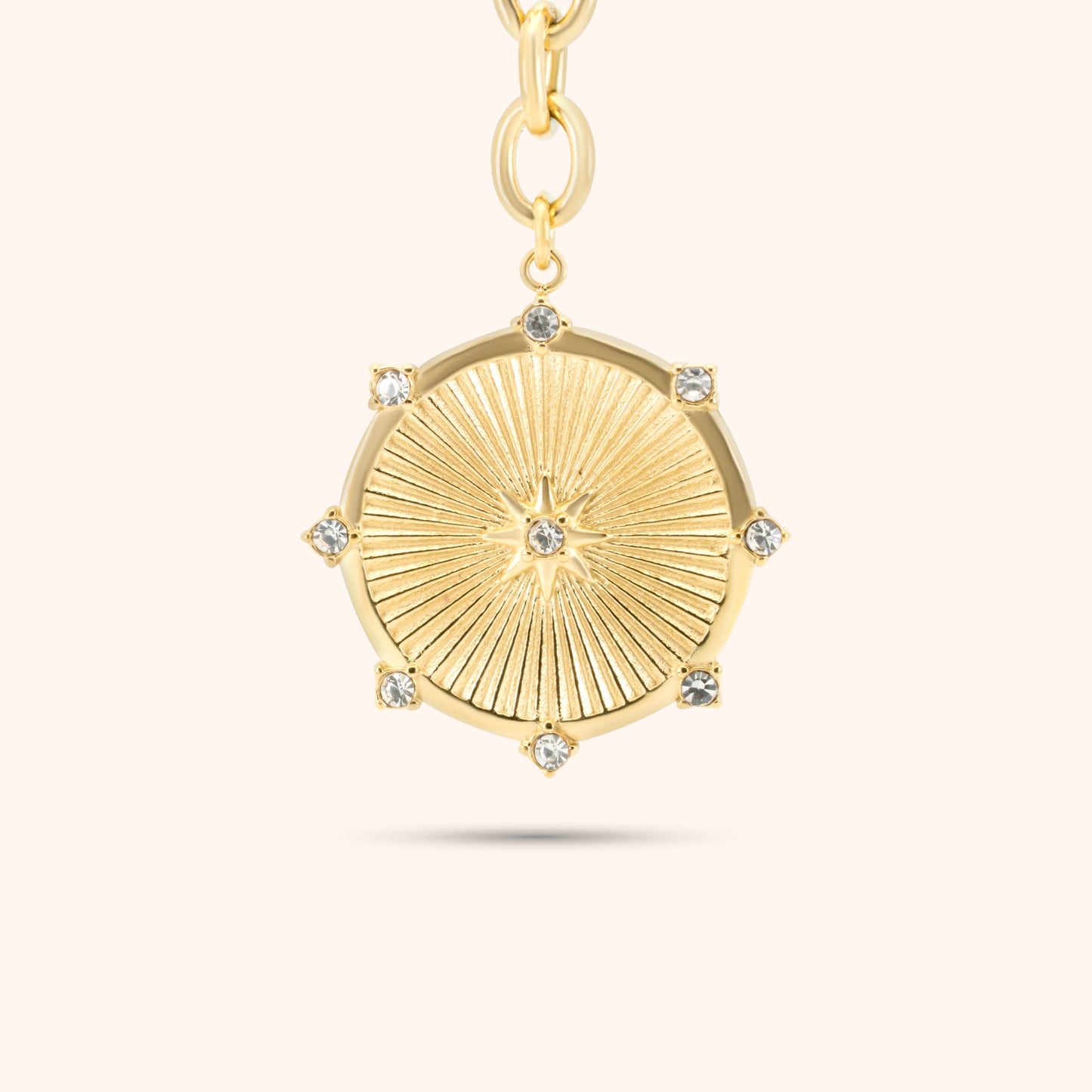 Close-up of the sunburst medallion pendant on the PRESSIE Radiant Heart Lariat necklace; 18k gold plated with radiating line texture, central star motif, and clear stone accents around the edge.