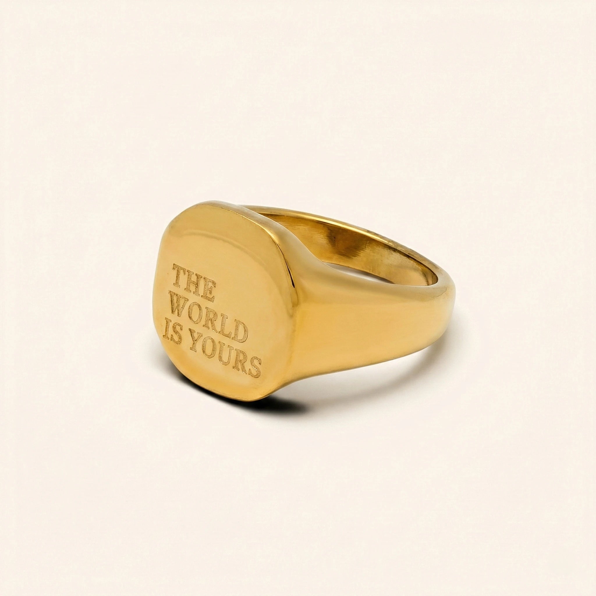 Gold ring with 'The World is Yours' engraving on a beige background