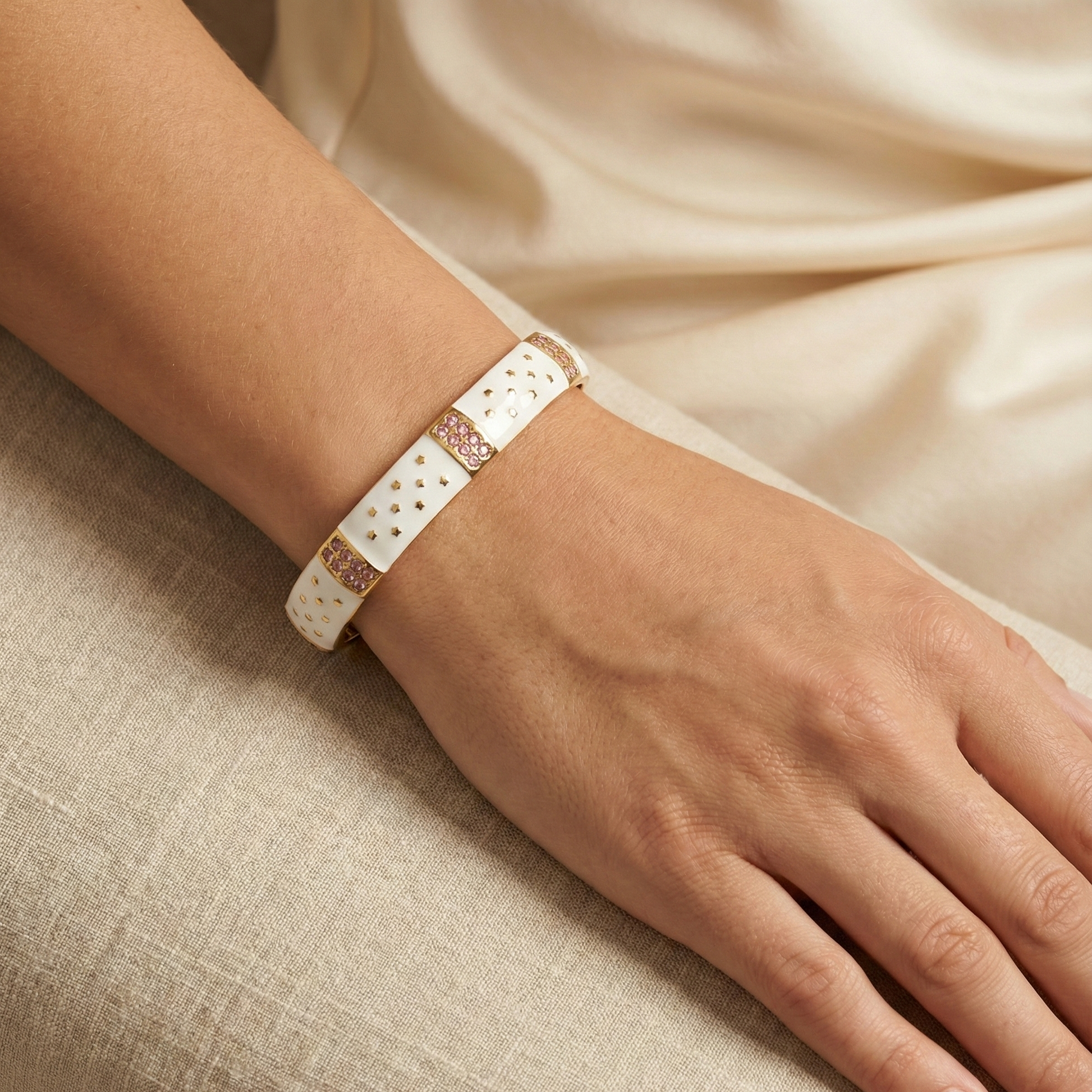 Close-up of a hand wearing a white bracelet with gold accents on a beige fabric background