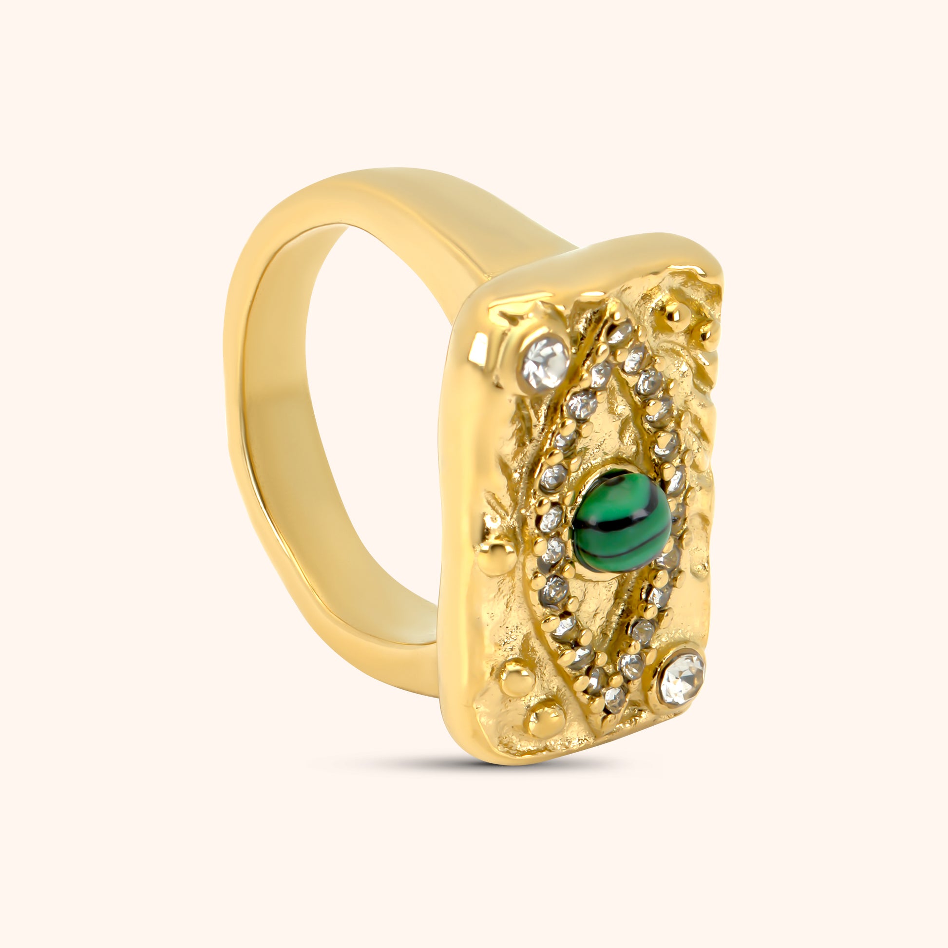 PRESSIE Sentinel Ring in 18k gold plate; angled view showing the rectangular face with evil eye design (green patterned stone, clear pavé stones) and the smooth, polished band.