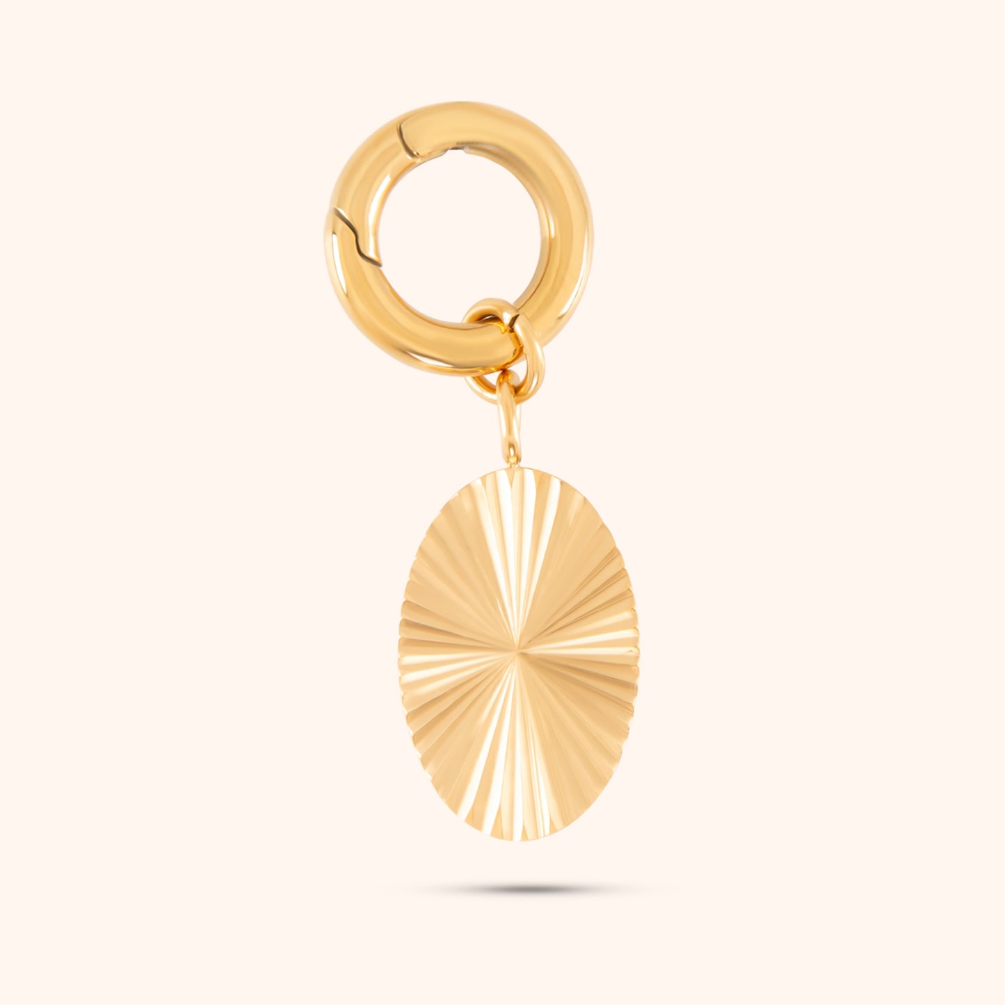 Close-up, angled view of a PRESSIE gold-plated, oval-shaped pendant with a highly faceted, light-reflecting surface. The pendant hangs from a small, circular gold hoop earring clasp.