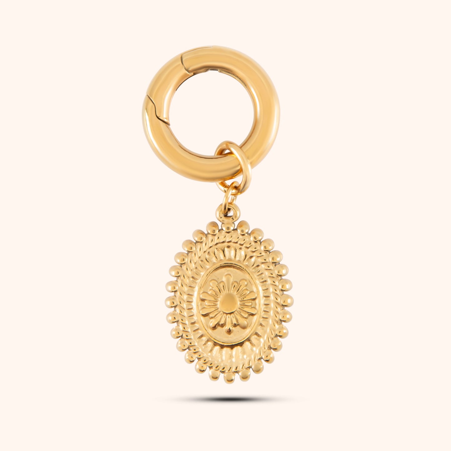 Close-up, angled view of a PRESSIE gold-plated, oval-shaped pendant hanging from a small, circular gold hoop earring clasp. The pendant features a textured border and a detailed, raised depiction of a landscape scene.