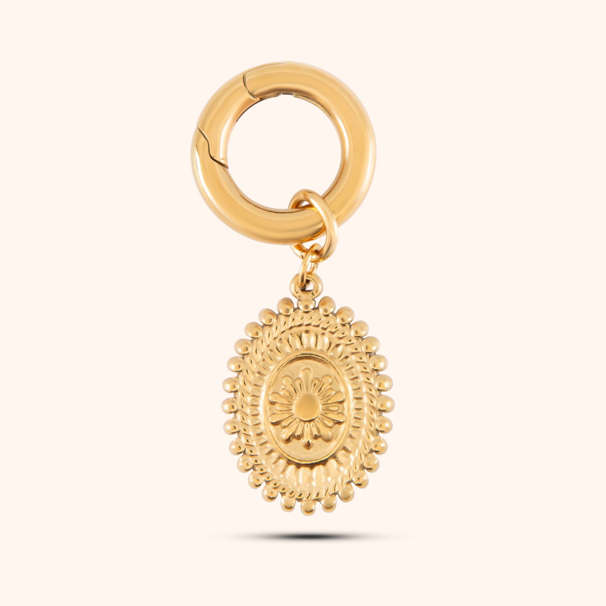 Close-up, angled view of a PRESSIE gold-plated, oval-shaped pendant hanging from a small, circular gold hoop earring clasp. The pendant features a textured border and a detailed, raised depiction of a landscape scene.