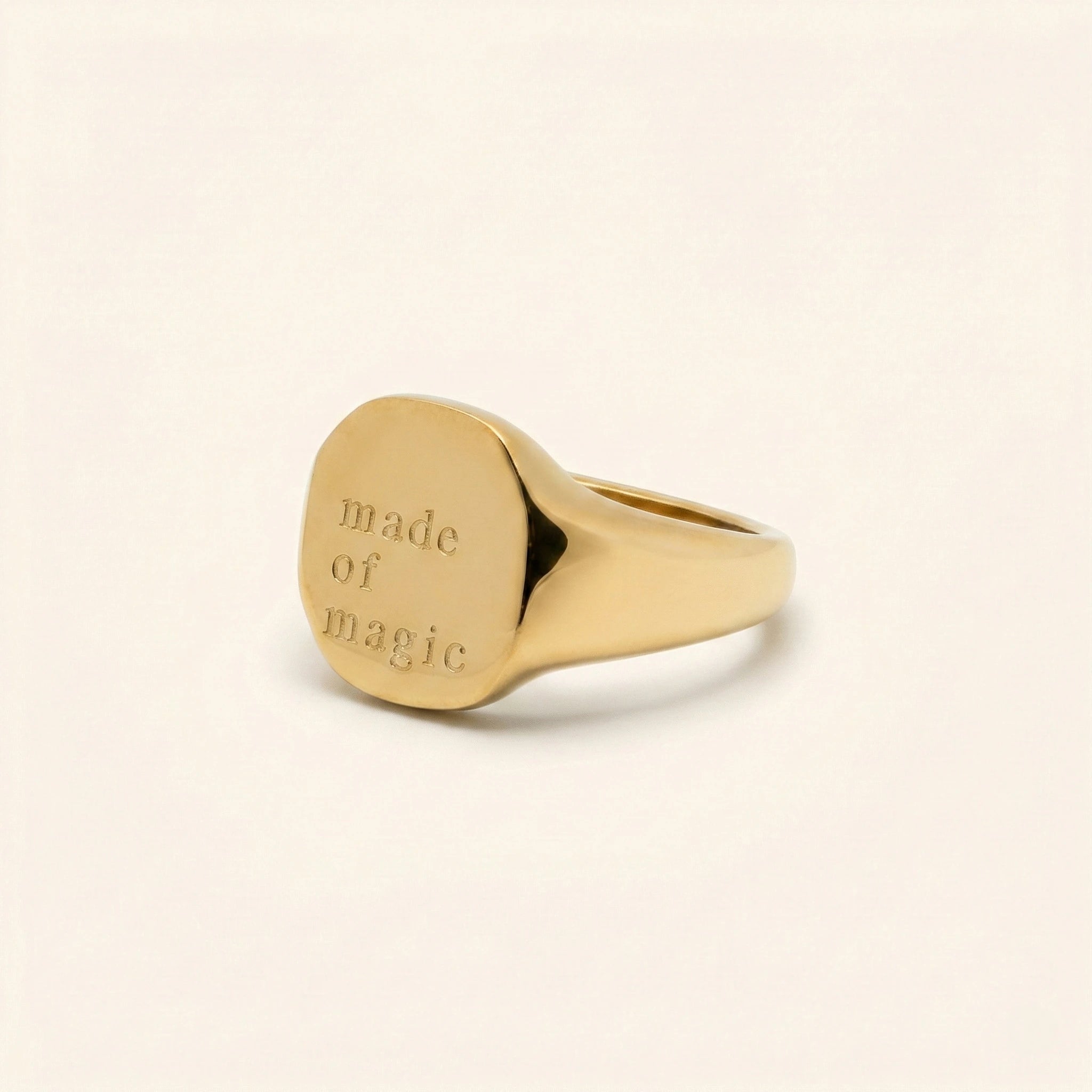 Gold ring with 'made of magic' engraving on a beige background
