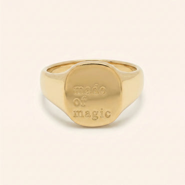 Gold ring with 'made of magic' engraving on a beige background