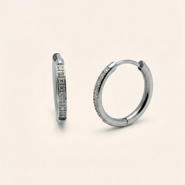 Pair of silver hoop earrings with embedded stones on a beige background