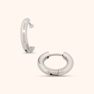 Detailed view of a small silver huggie earring, highlighting its sleek and versatile style.
